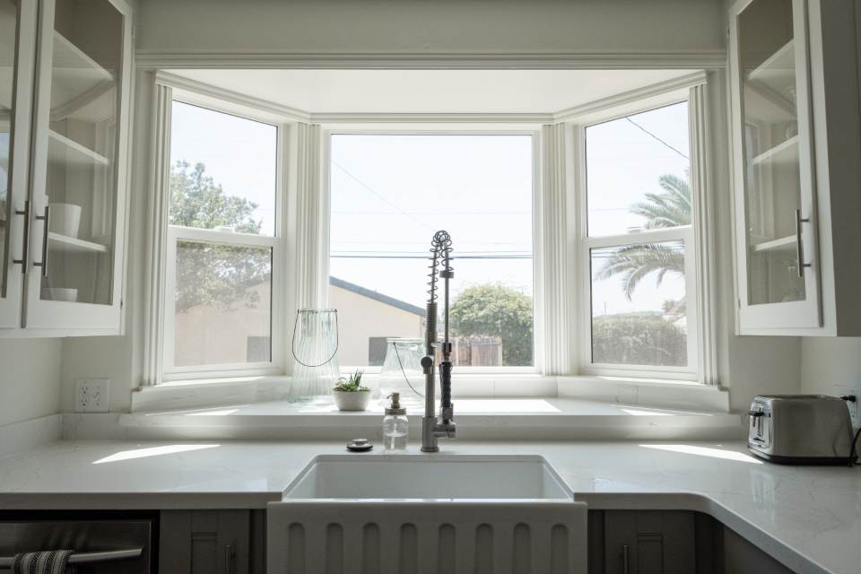 White cabinets around a farmhouse sink under a bay window